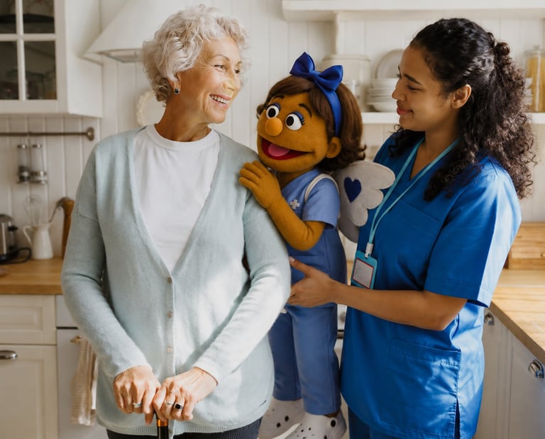 Healthcare worker in blue scrubs interacts with elderly woman and Muppet-style puppet character in kitchen setting